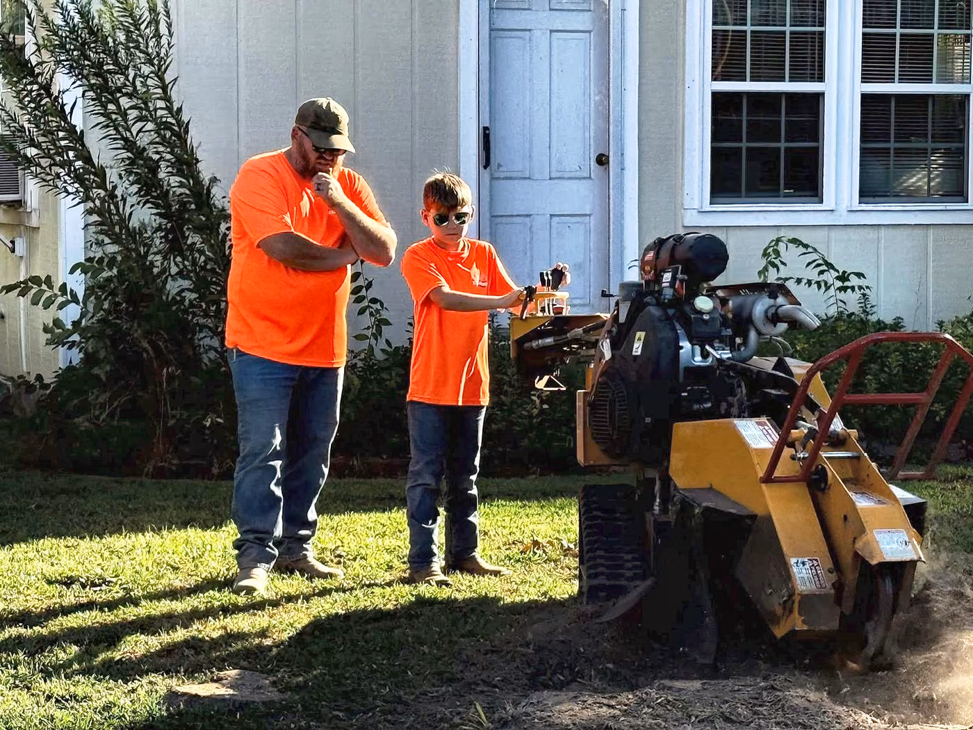 Chris Stackler and his son at the controls of the KCL Outdoors stump grinder beside a customer's house