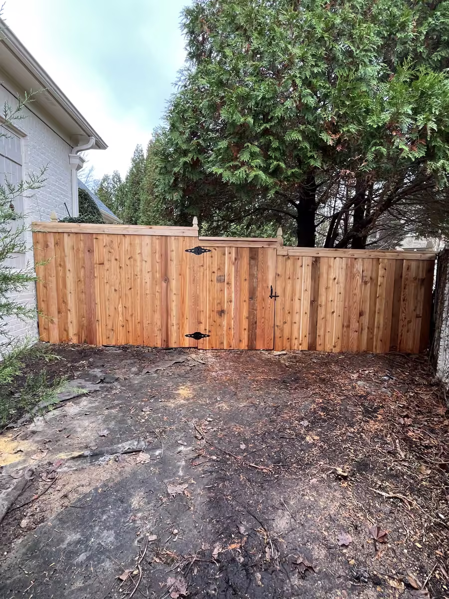 A new cedar privacy fence with a double gate beside a house, the ground in front freshly cleared