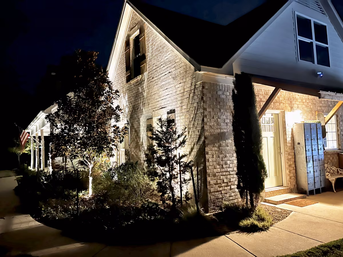 A brick house at night with landscape lighting on the trees, the columns and the front walk
